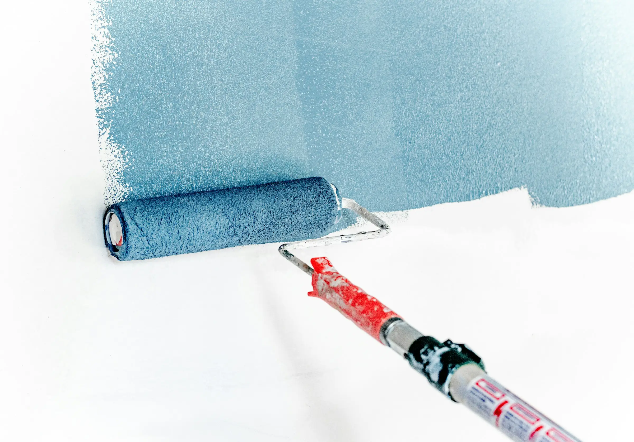 Farbroller trägt blaue Farbe auf eine weiße Wand auf
